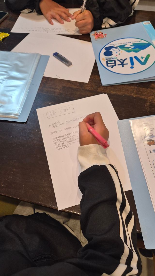 위에서 찍은 모습. 아이가 분홍 펜으로 이야기 글을 쓰고 있다. 옆에 ‘AI太白’ 파일이 있다.